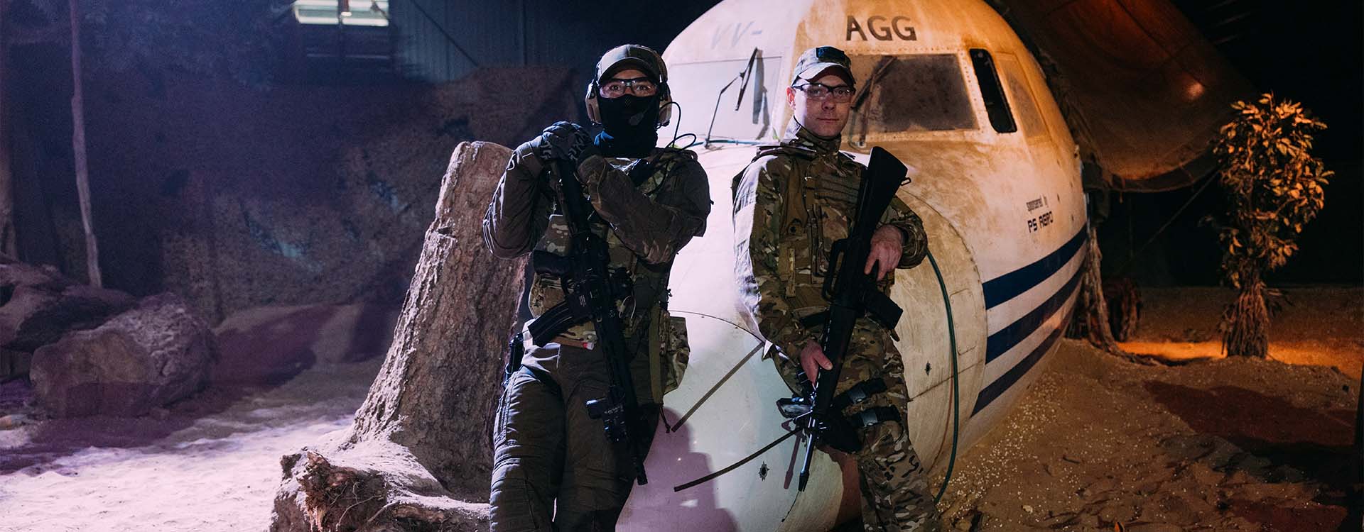 Twee airsofters met replica bij een vliegtuig op een indoor skirm locatie.