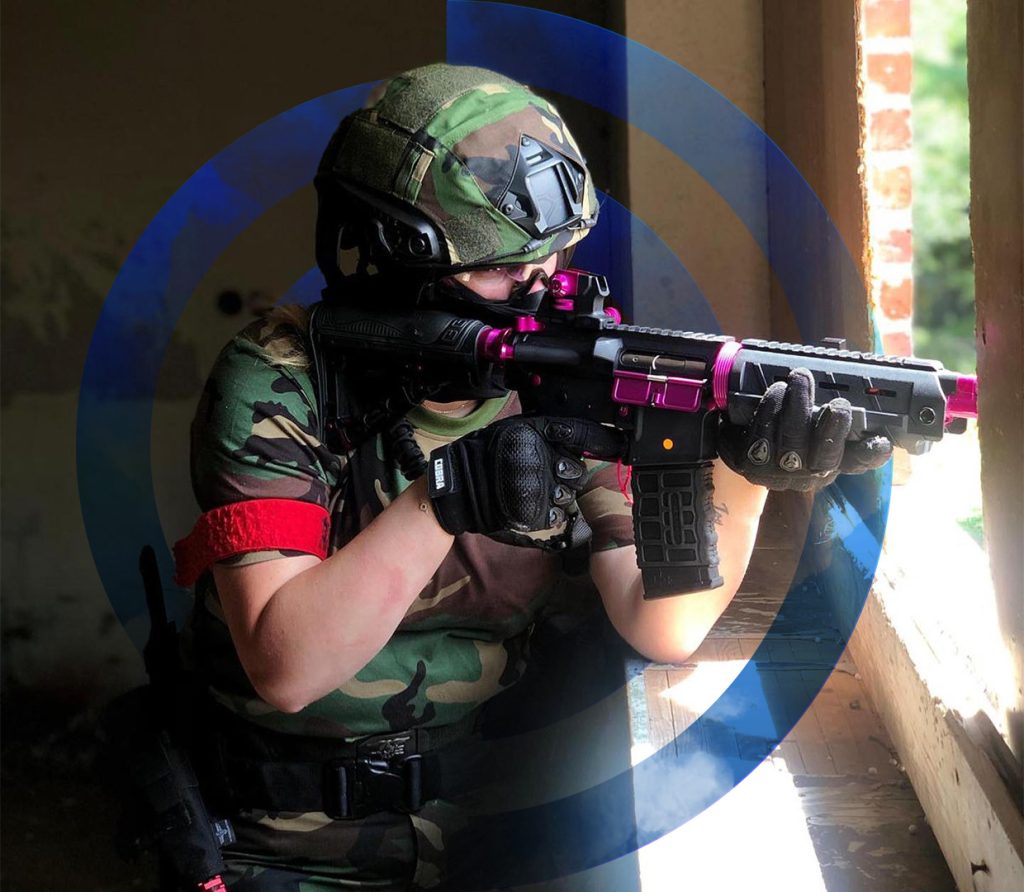 Airsofter tijdens een skirm op een buitenlocatie, mikkend naar buiten vanuit een gebouw